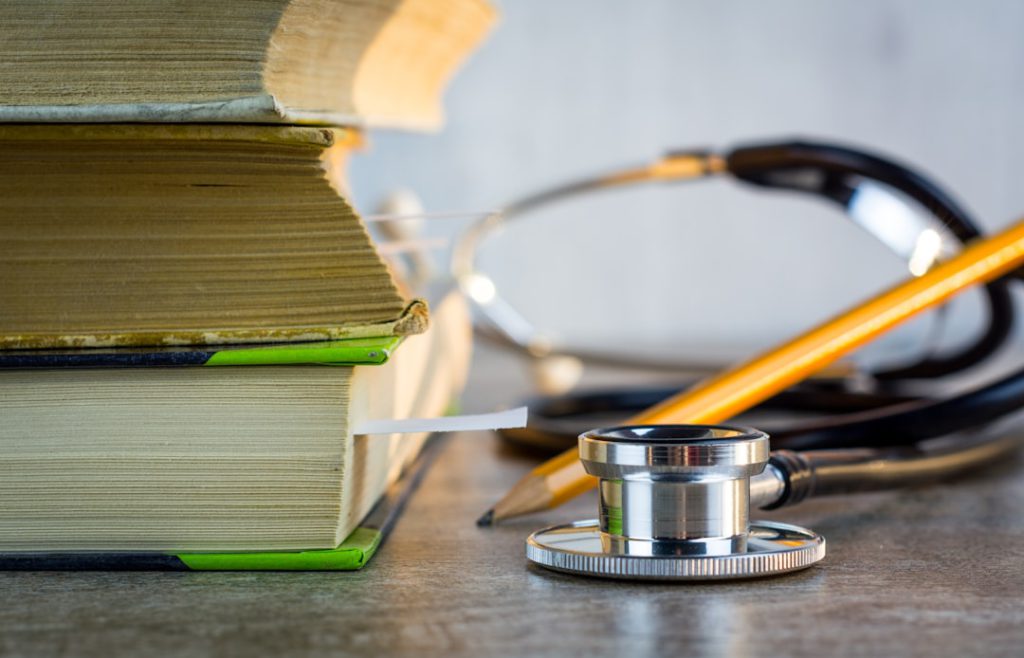 Close-up of stacked textbooks, a stethoscope, and a pencil on a surface, emphasizing academic tools.