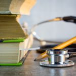 Close-up of stacked textbooks, a stethoscope, and a pencil on a surface, emphasizing academic tools.