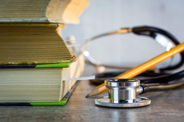 Close-up of stacked textbooks, a stethoscope, and a pencil on a surface, emphasizing academic tools.